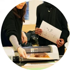 Two people in a workshop printing drawings.